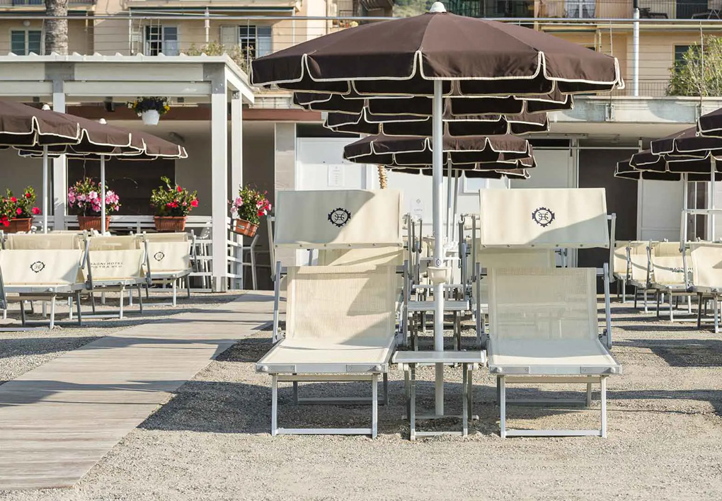 file ordinate di ombrelloni sulla spiaggia. una passerella corre dall'ingresso verso la riva. L'entrata è decorata con colorati vasi di fiori, sullo sfondo i palazzi della passeggiata