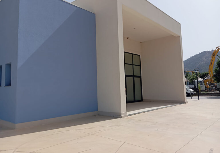 Edificio moderno con ingresso coperto, ampia pavimentazione esterna a livello e accesso privo di gradini.