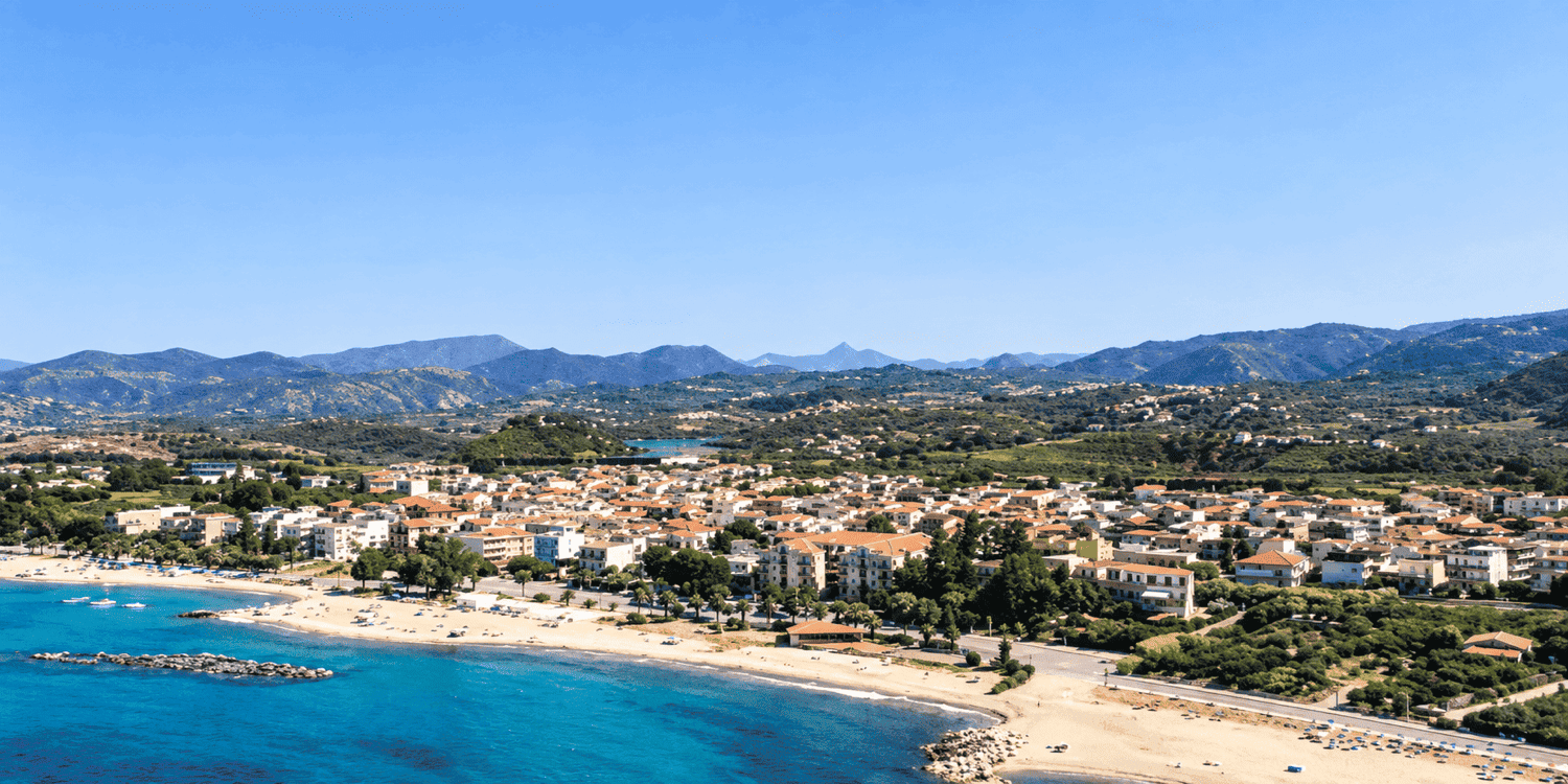 Veduta panoramica di Falcone: il centro abitato si estende lungo un’ampia spiaggia di sabbia chiara, affacciata sul mare turchese e circondata da colline e montagne verdeggianti.