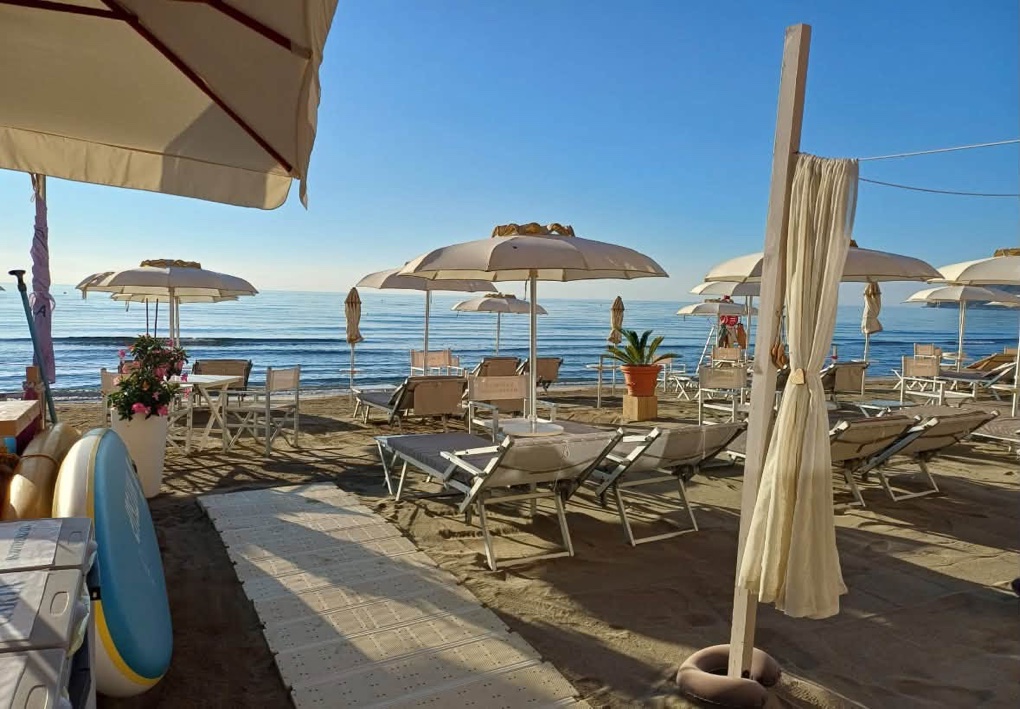 Spiaggia attrezzata con lettini e ombrelloni, passerella sulla sabbia e mare sullo sfondo.