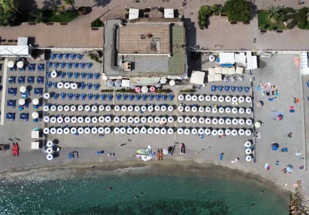 Vista aerea dello stabilimento balneare, con file ordinate di lettini e ombrelloni, la spiaggia e il mare.