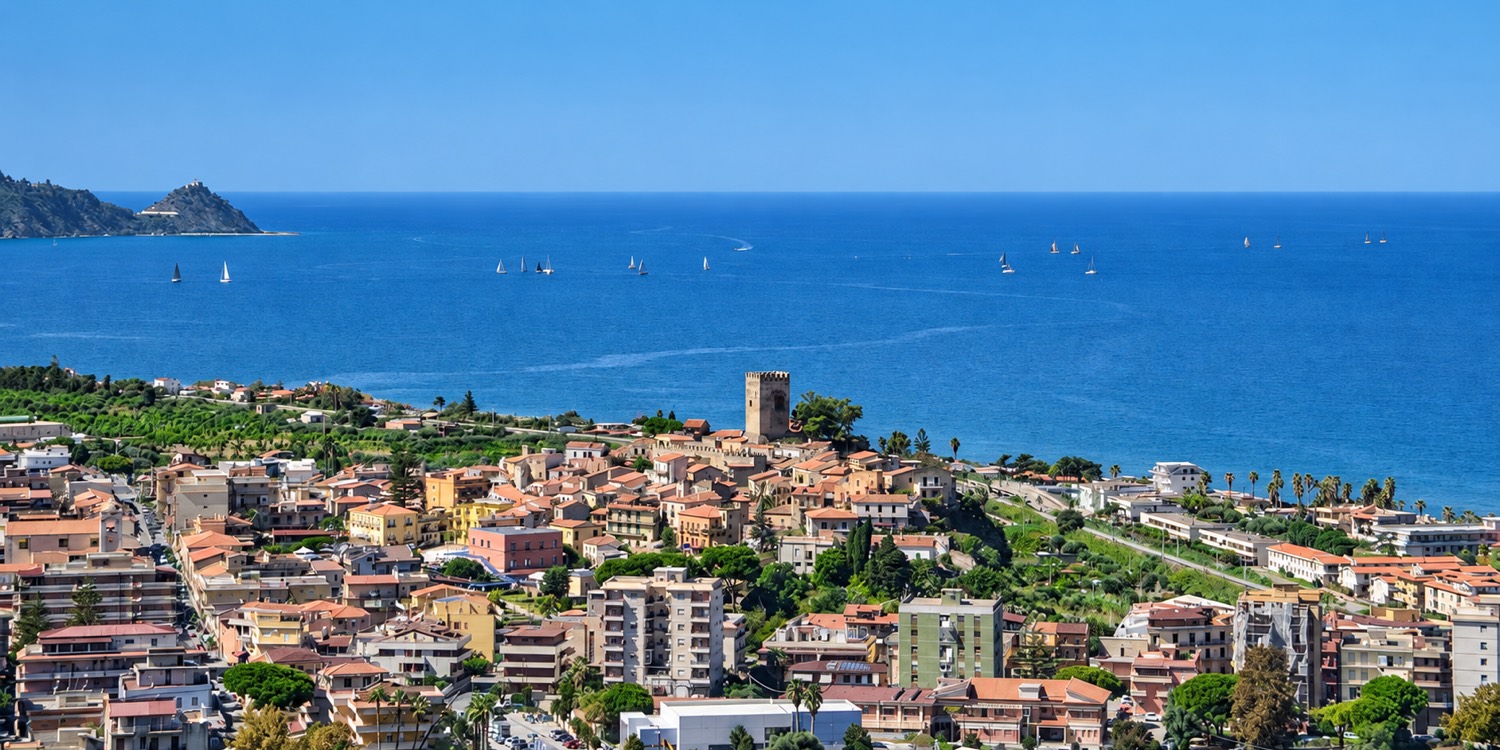 Vista panoramica di Brolo, in Sicilia, con il borgo e il castello medievale affacciati sul mare, sul quale navigano diverse barche a vela.